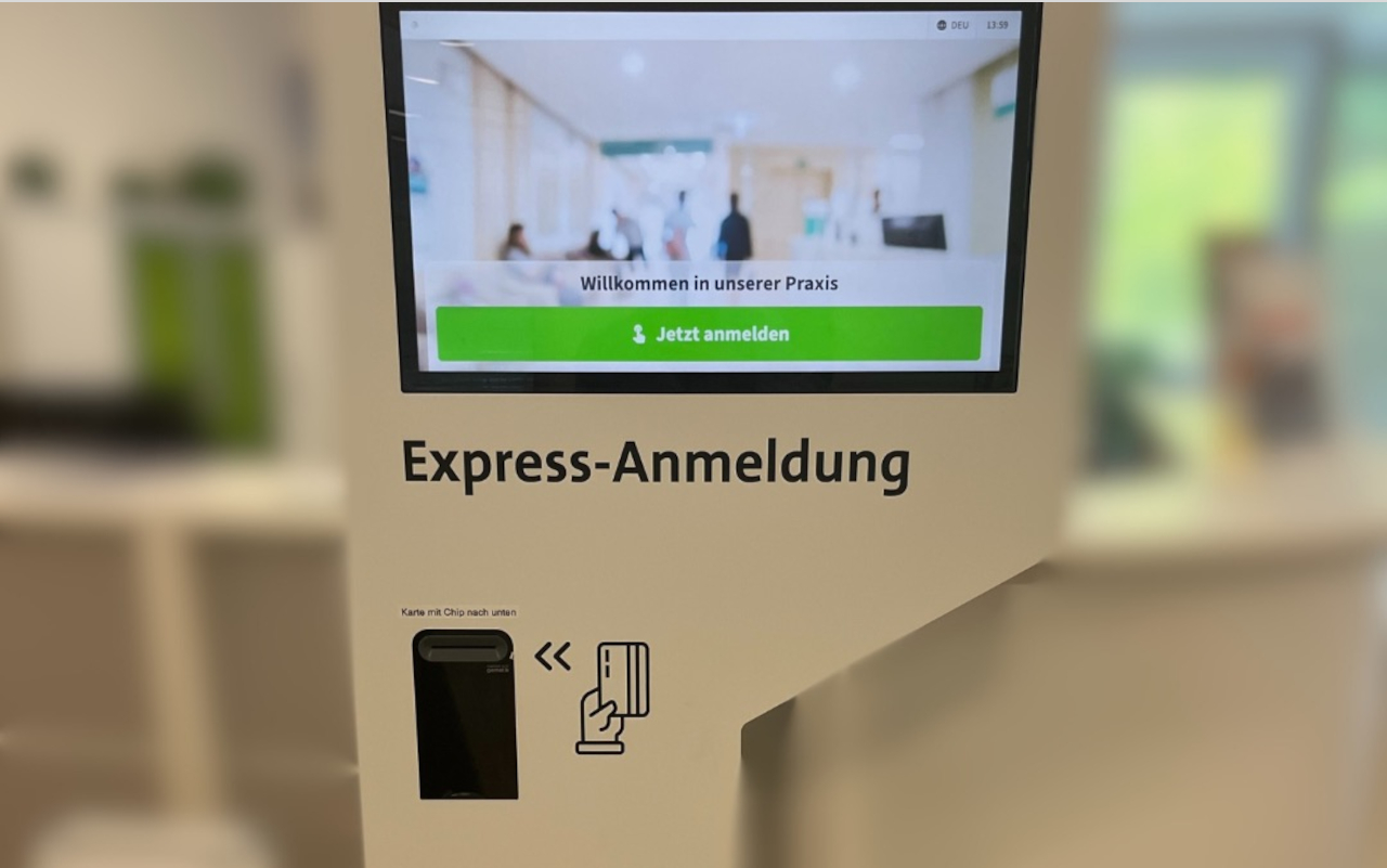 Express-Anmeldung Ein Foto von der "Express-Anmeldung, einer Säule mit Monitor und Fach für den Karteneinschub. Der Tresen steht im Hintergrund in einiger Entfernung. Auf dem Monitor steht: "Herzlich willkommen in unserer Praxis. Jetzt anmelden."